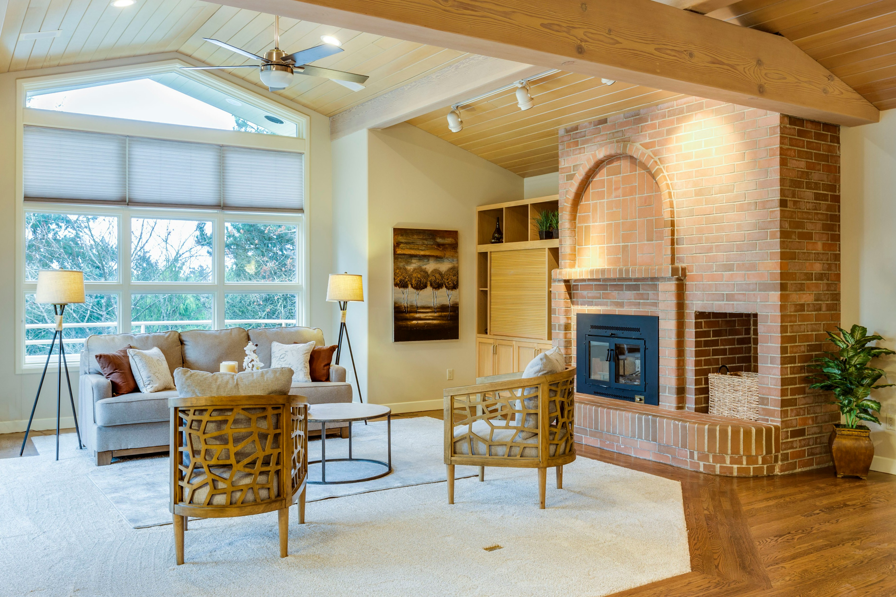 Rustic living room with arched brick fireplace, wood-beam ceiling, and lattice accent chairs