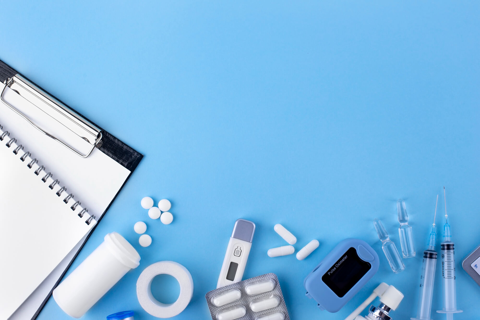 Mavi zemin üzerinde termometre, ilaçlar, şırınga ve medikal ekipmanlar.