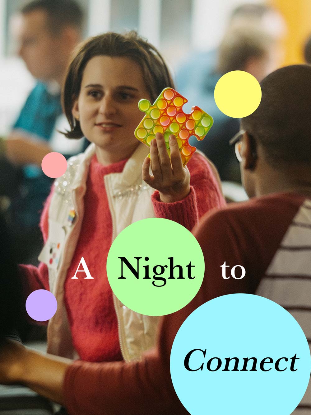 A young person holds up a colorful puzzle-piece fidget toy while talking with another attendee during a Community Autism Resources social event.