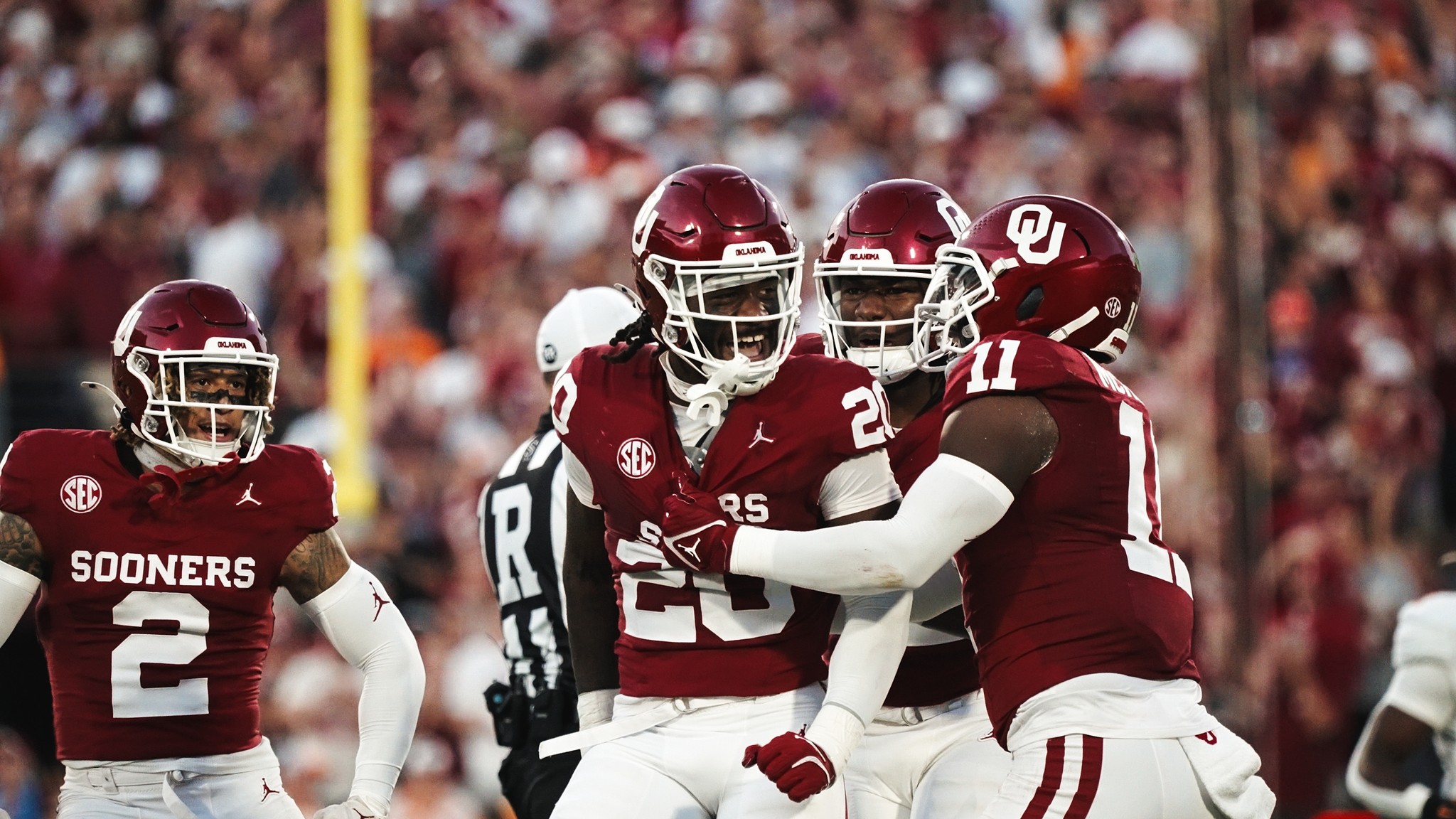 Three Oklahoma Sooners football players celebrating on the field during a game, wearing crimson and cream uniforms.