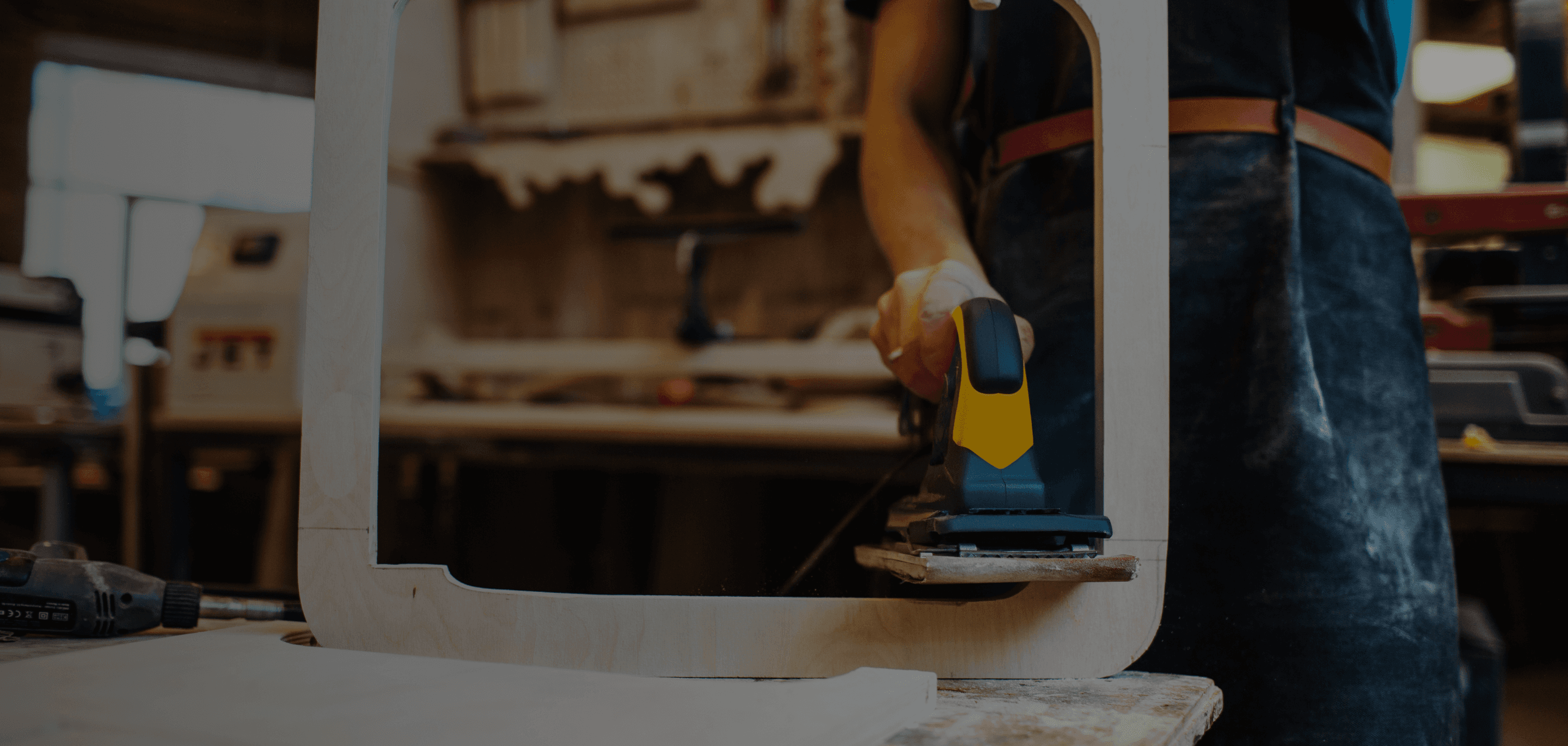 Un employé décape un meuble en bois à l'aide d'une ponceuse.