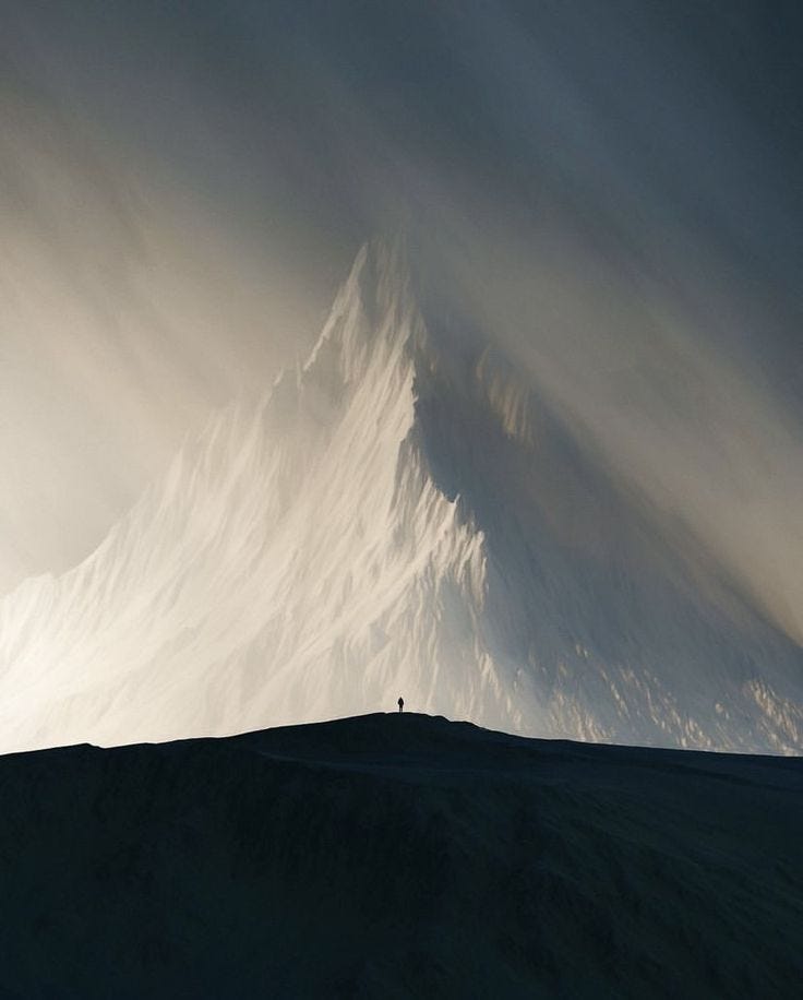 This may contain: a person standing on top of a hill under a cloudy sky with a mountain in the background