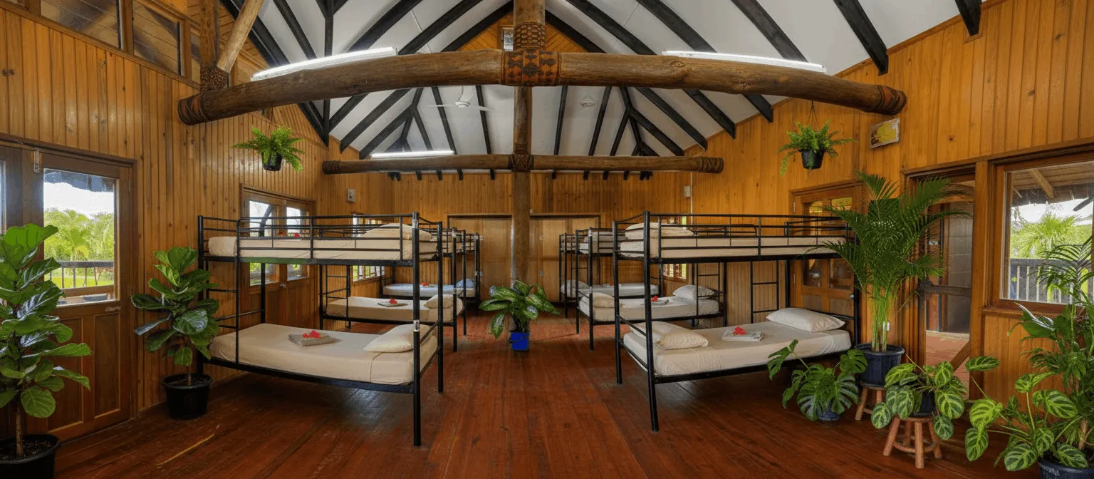 A bright, spacious dorm room at Uprising Beach Resort with several bunk beds, wooden walls, and tropical plants.