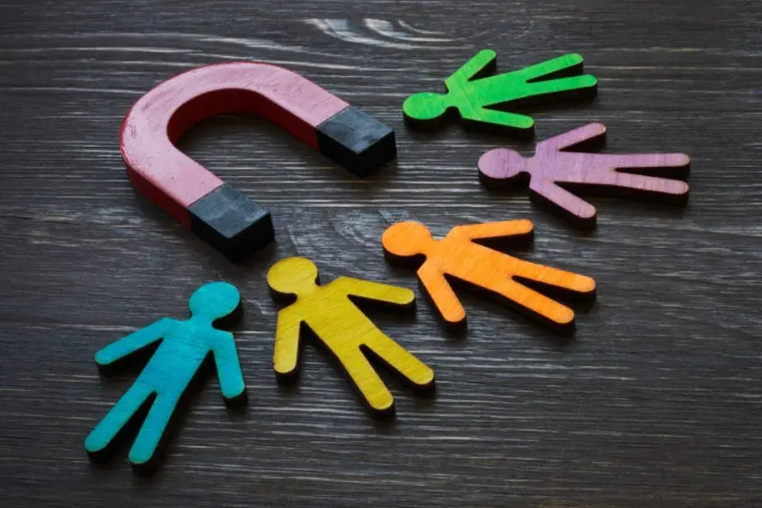 Red horseshoe magnet attracting colorful stylized figures on a dark wooden background, symbolizing customer acquisition.
