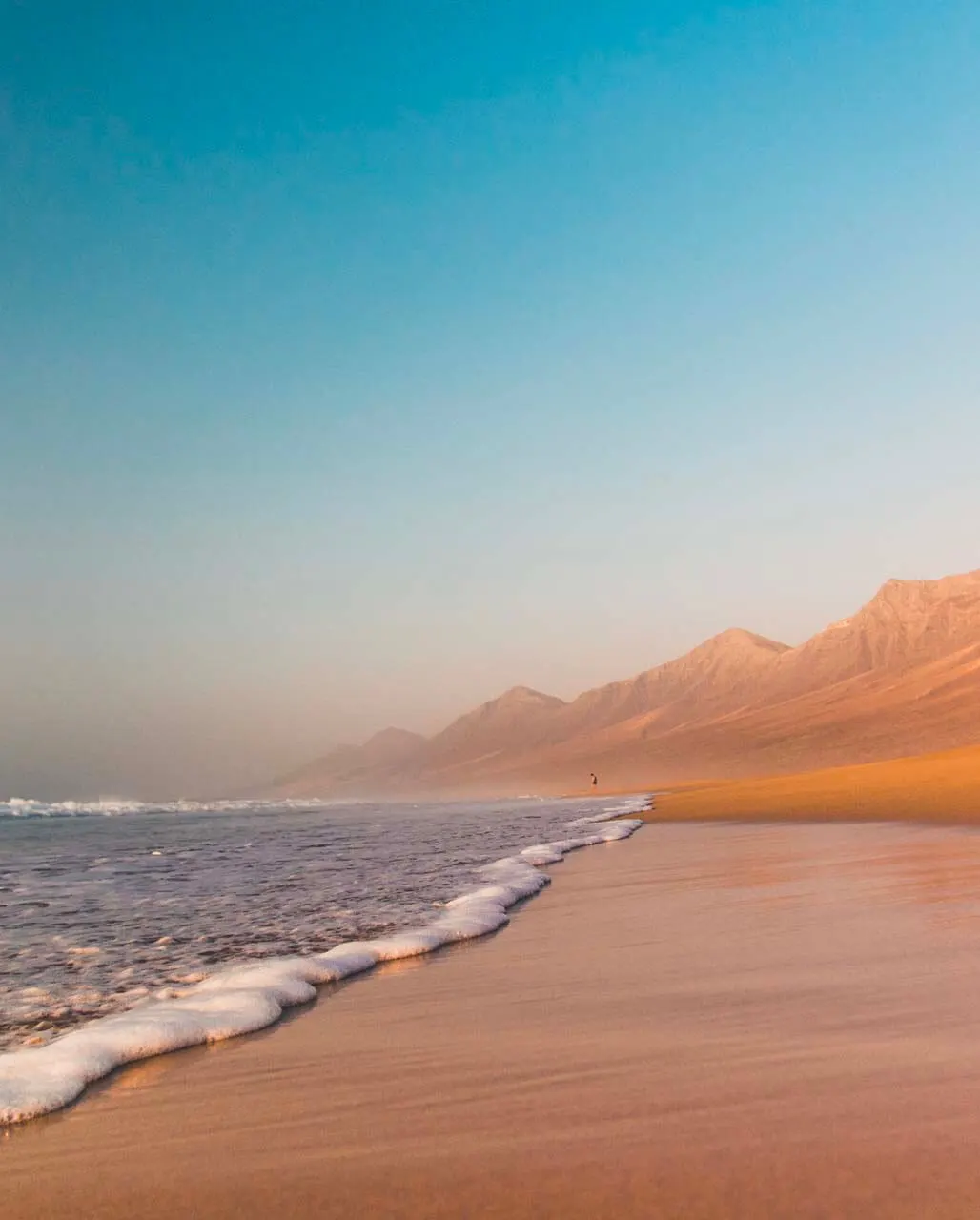 Serene beach scene with gentle waves, golden sand, and soft, colorful sky at sunrise.