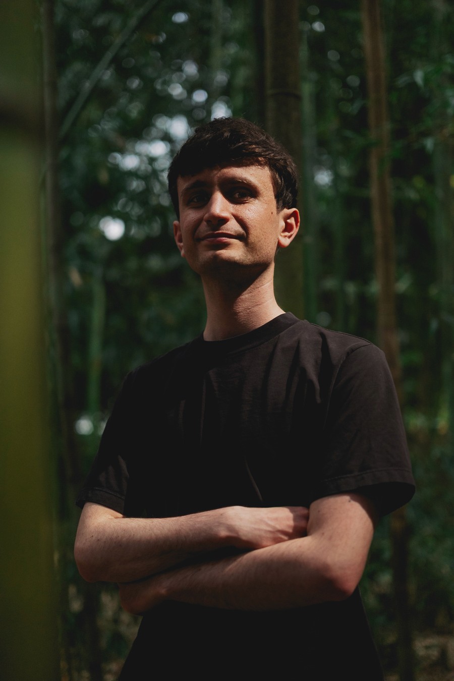 Um retrato médio de Matteo Folesani em pé com os braços cruzados em uma floresta de bambu, iluminado por uma luz solar quente e filtrada.