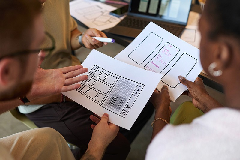 Team collaborating on mobile app wireframes, reviewing sketches of screens and layout designs.