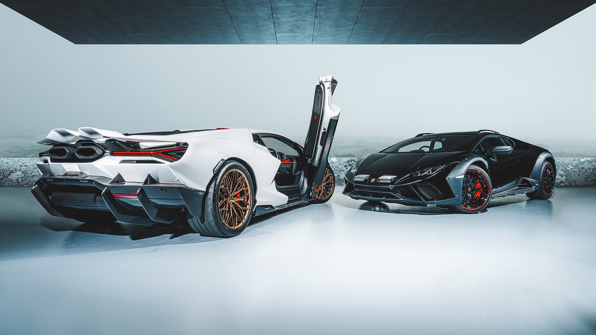 White Lamborghini Revuelto with one scissor door raised, shown from the rear three-quarter beside a black Lamborghini Huracán Sterrato in a cool-toned studio, the Revuelto's bronze wheels and Y-shaped taillights and the Sterrato's red-accented wheels and raised stance in frame, on a glossy reflective floor.