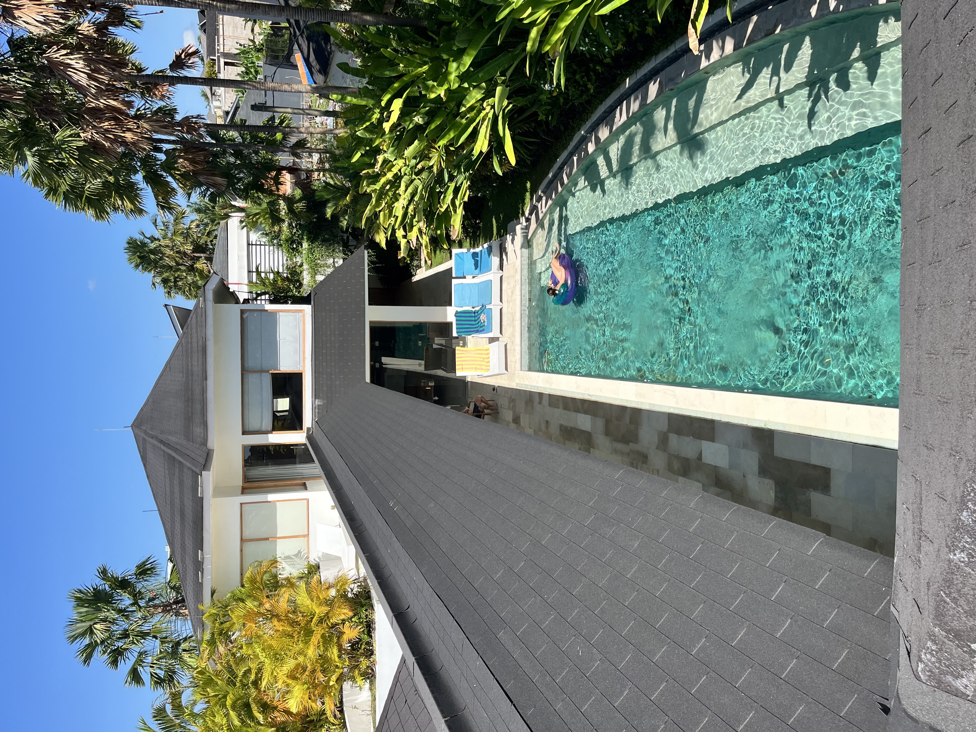 A smiling woman with her arms crossed, standing against a dark green background. She has long, dark hair.