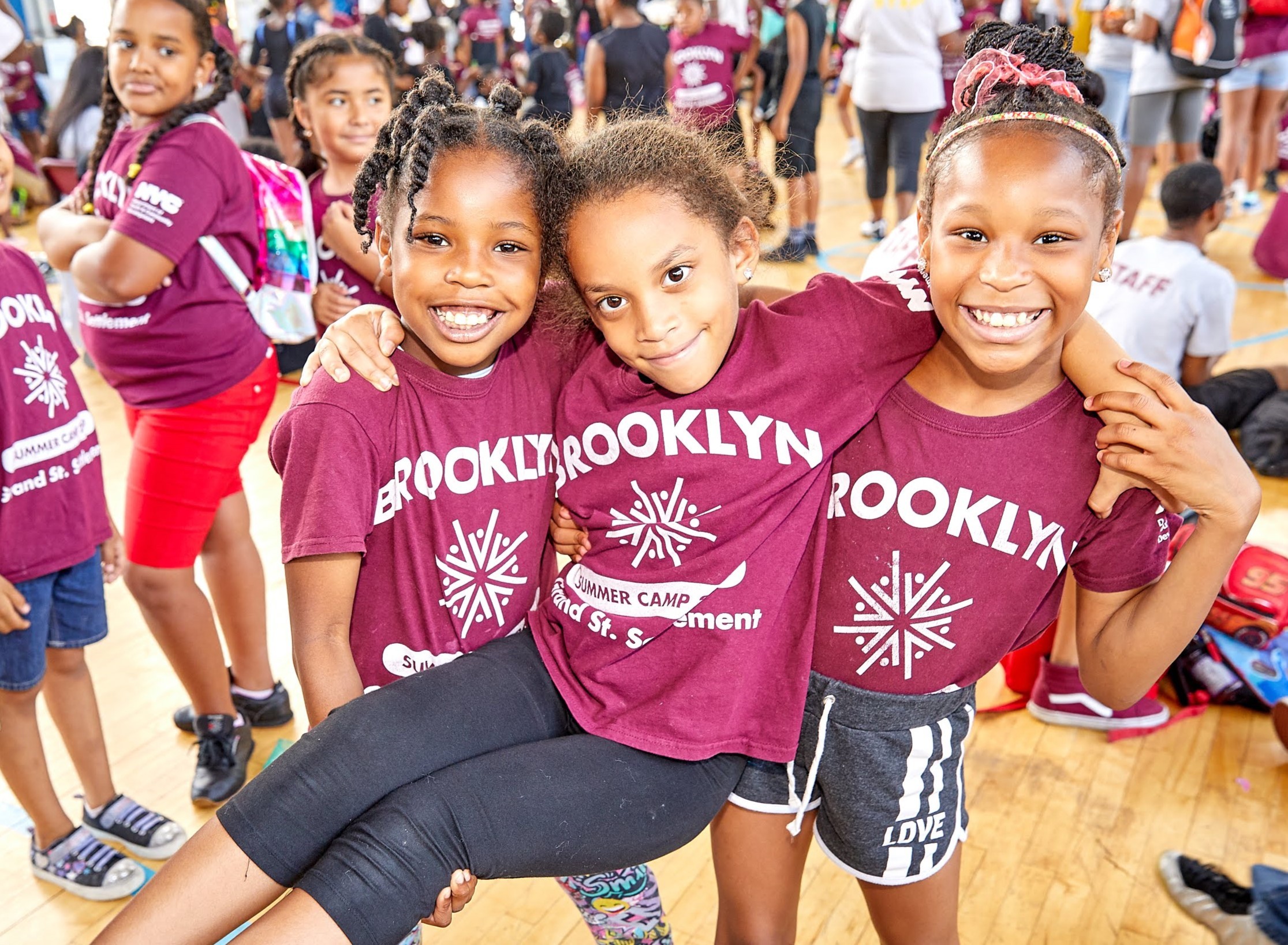 Two young girls hold up another in a gymnasium during a summer camp event.