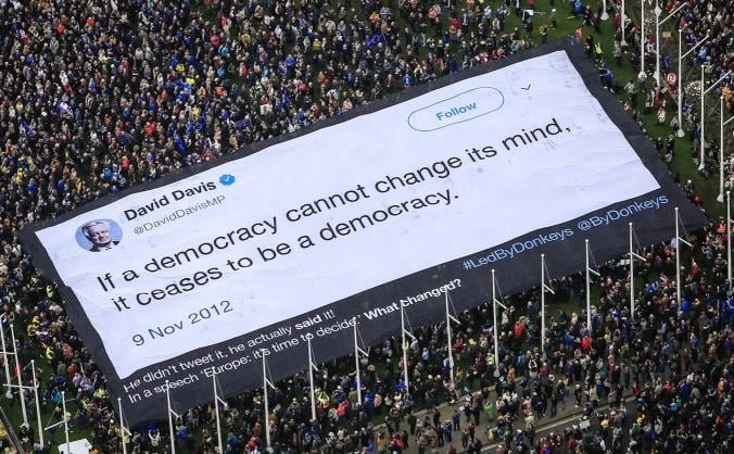 photo taken from above, of a crowd marching. Above them, a big canva on which is printed a quote from David Davis: 'if a democracy cannot change its mind, it ceases to be a semocracy.' Underneath, the caption 'he didn't tweet it, he actually said it!!! and the hashtags #:edByDonkeys