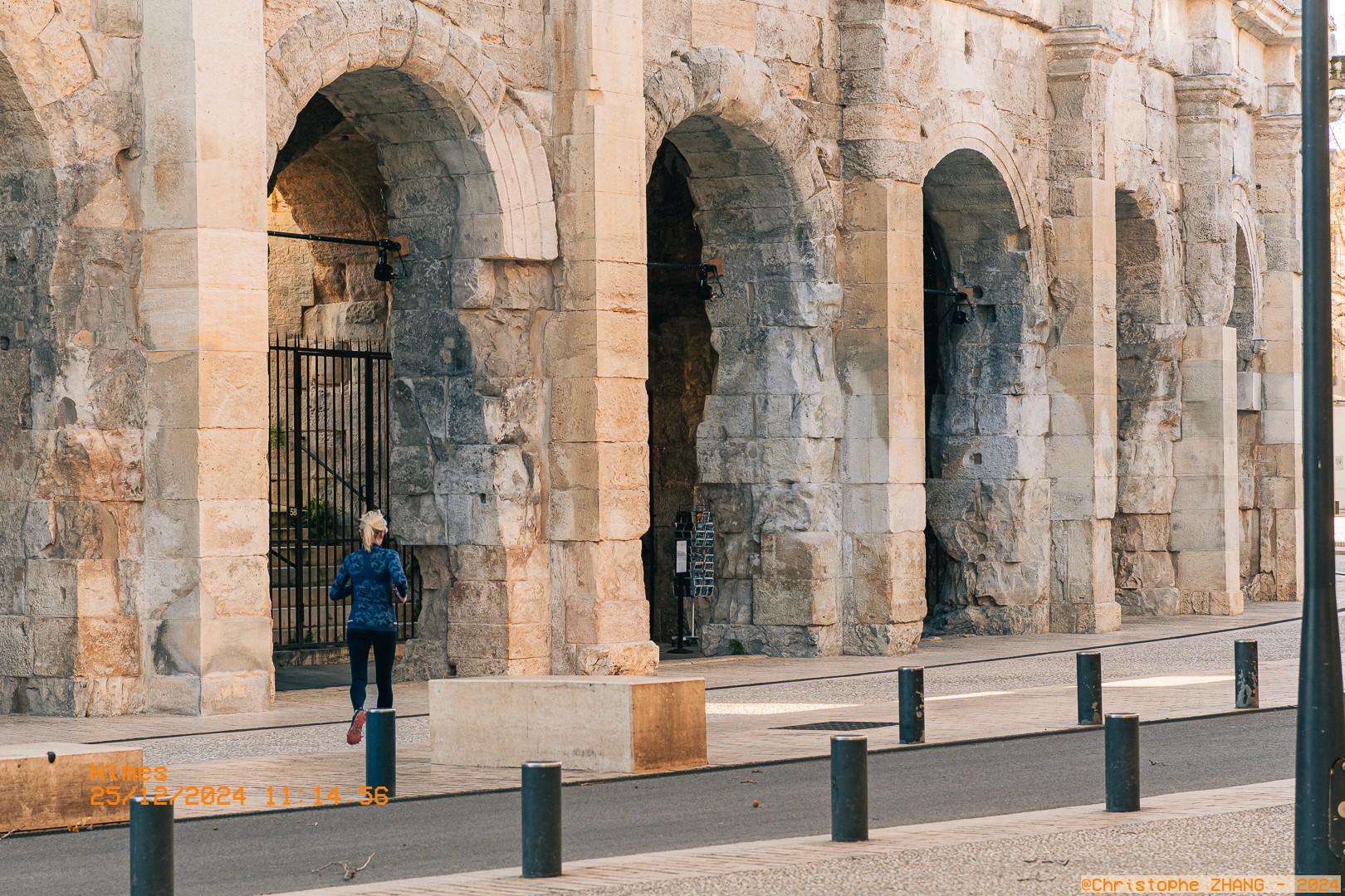 Scène urbaine devant les arènes de Nîmes, avec une femme courant le long du monument.