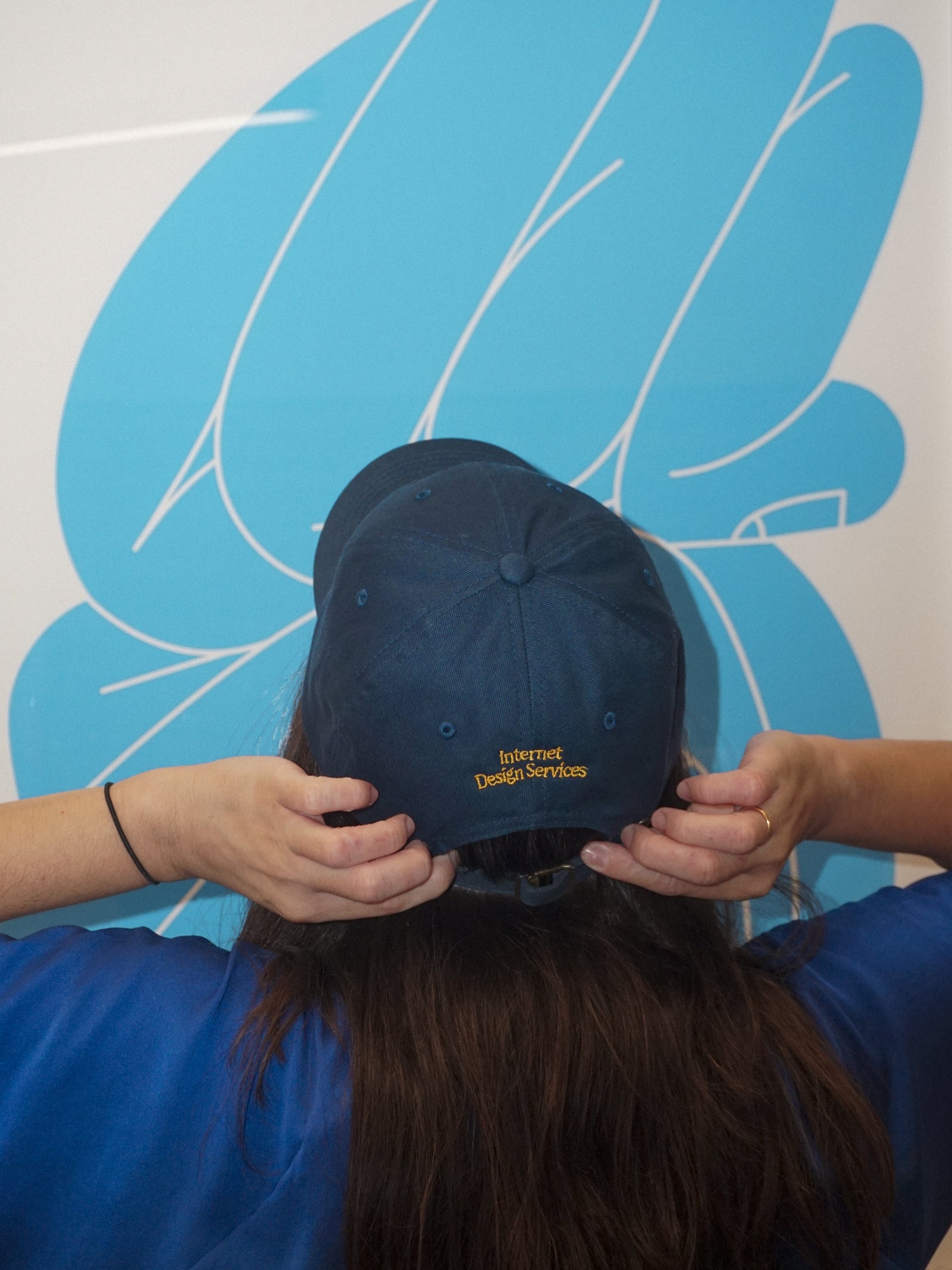 Person holding a navy blue cap with yellow text against a blue and white abstract background