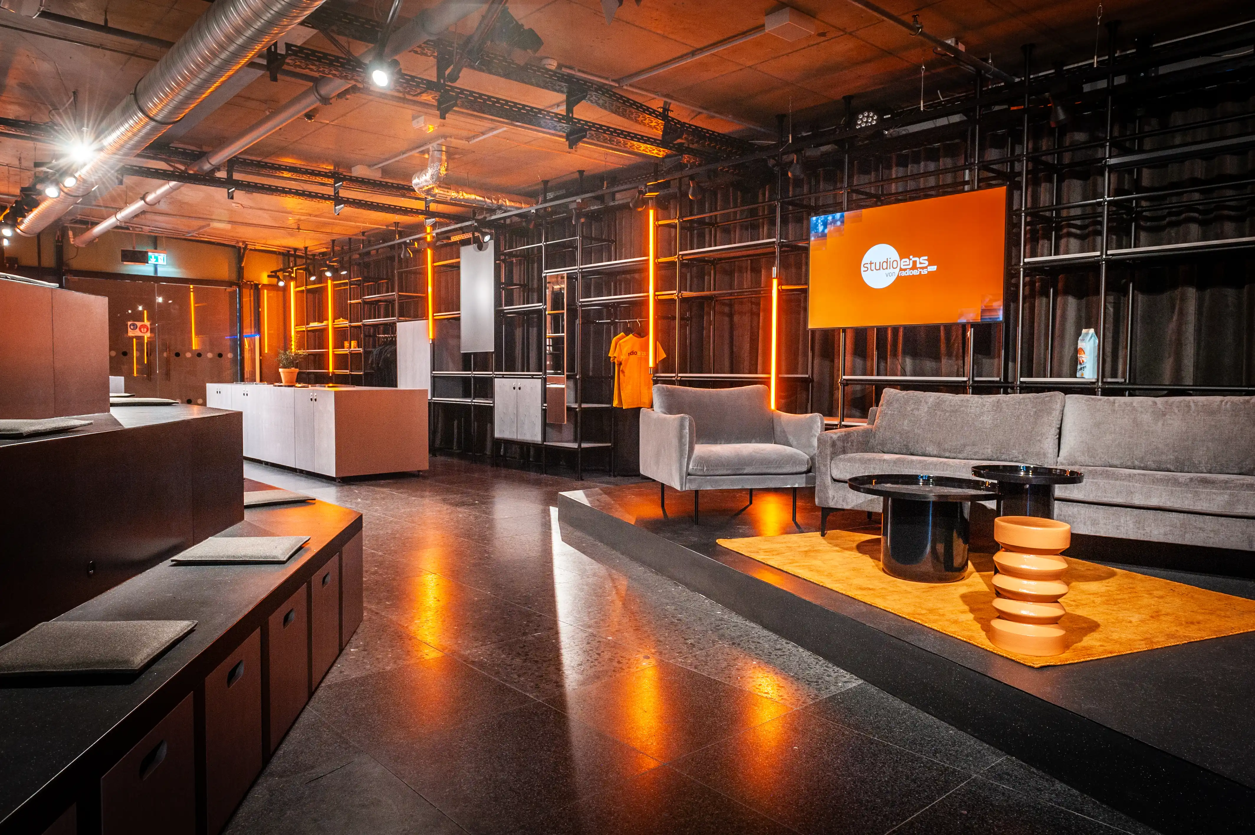 Lounge corner of the Radio Eins studio with grey sofas, orange checkerboard screen and ribbed terracotta side table.