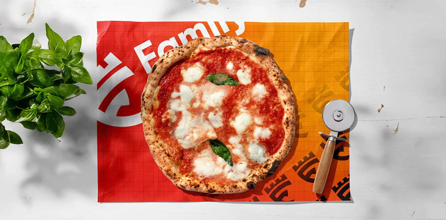 A freshly baked pizza served on a branded Family City placemat with a pizza cutter and basil leaves beside it.