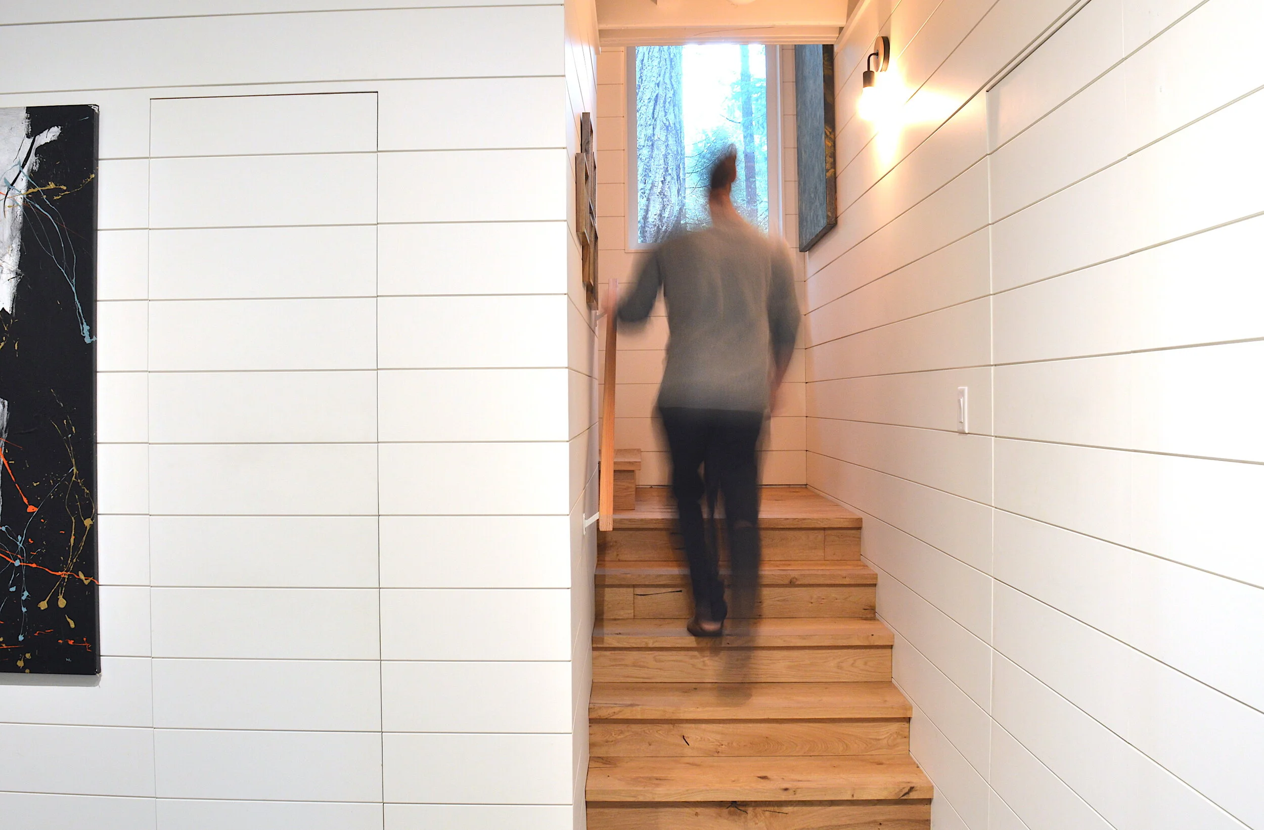 Modern two-story home with large glass windows, warmly lit interiors, and a balcony. Surrounded by trees and a manicured lawn at dusk. Cozy ambiance.