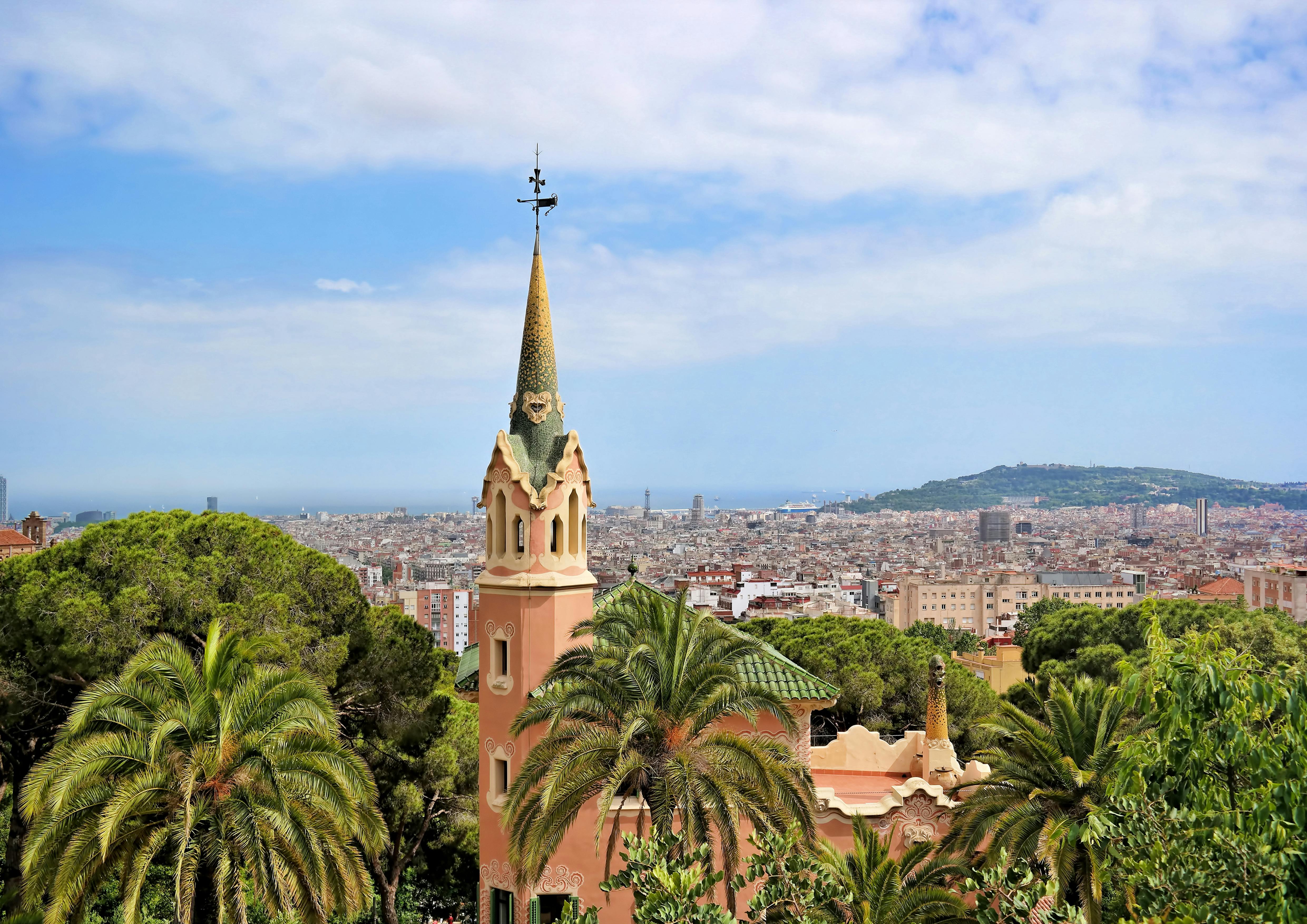 Uitzicht over de stad Barcelona vanaf Parc Güell, met groene bomen en een panoramisch uitzicht op de stad.