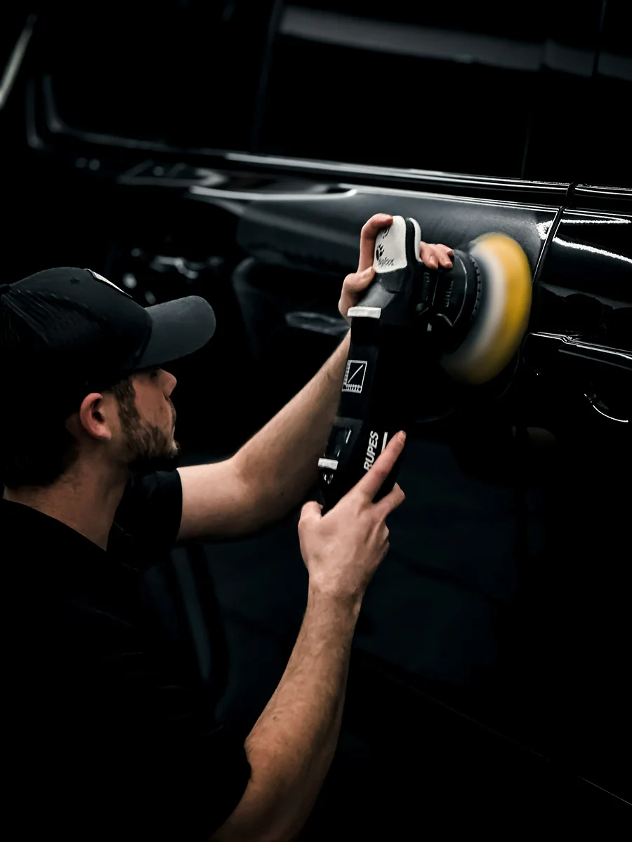 Professional detailer performing machine polishing on a luxury vehicle exterior.