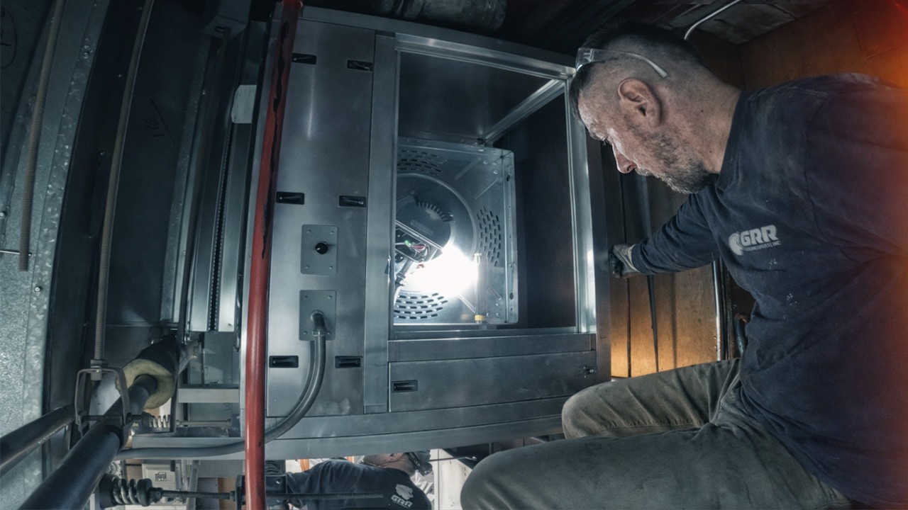 GRR technician inside tight-access air handling unit during HVAC retrofit with EC motor fan system installation