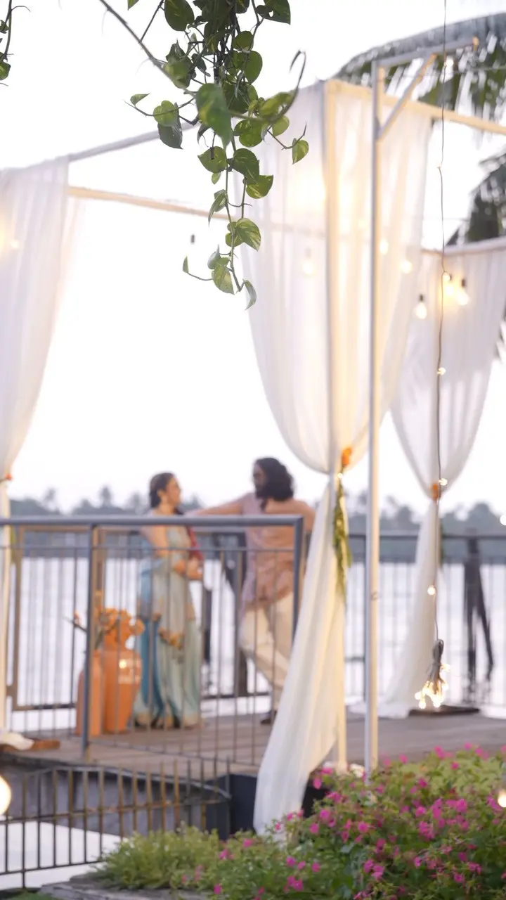 Couple in traditional attire beneath draped fabric and string lights on the riverside deck at Vedic Village Kodungallur at dusk