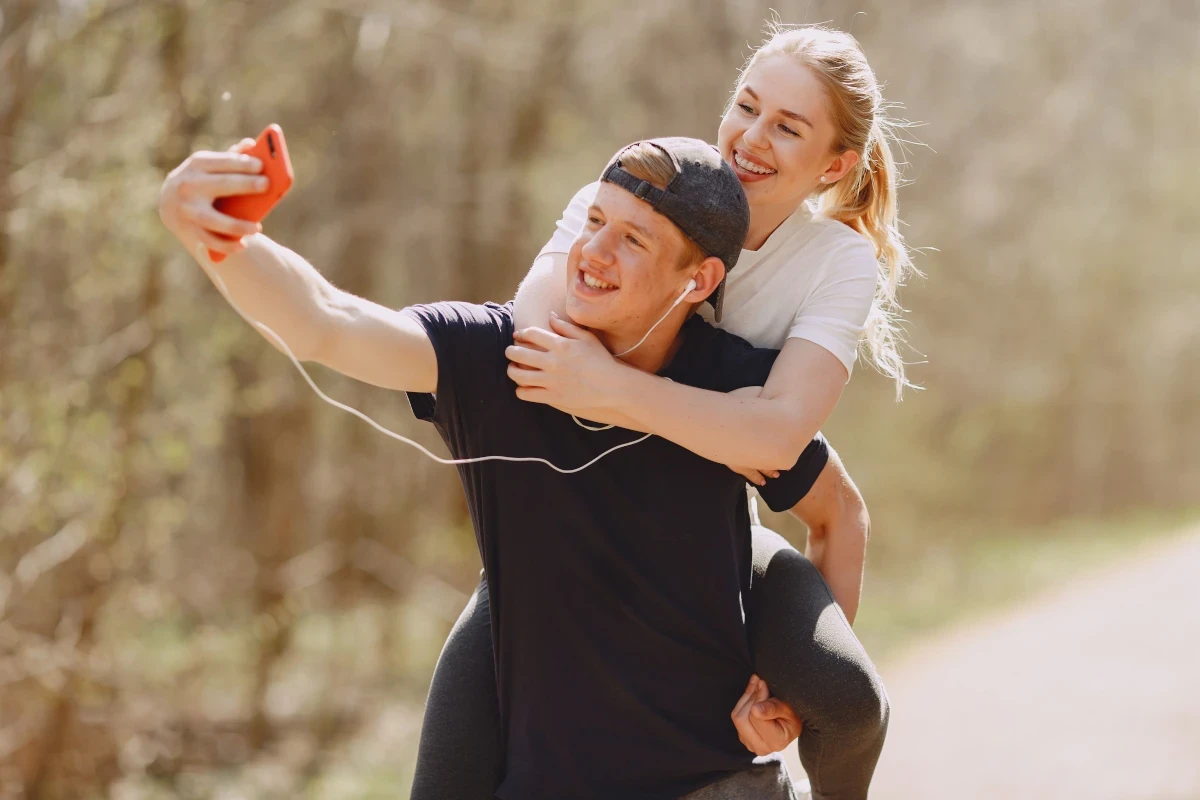 Smiling young couple outdoors, with the woman riding piggyback as they enjoy a carefree moment together.