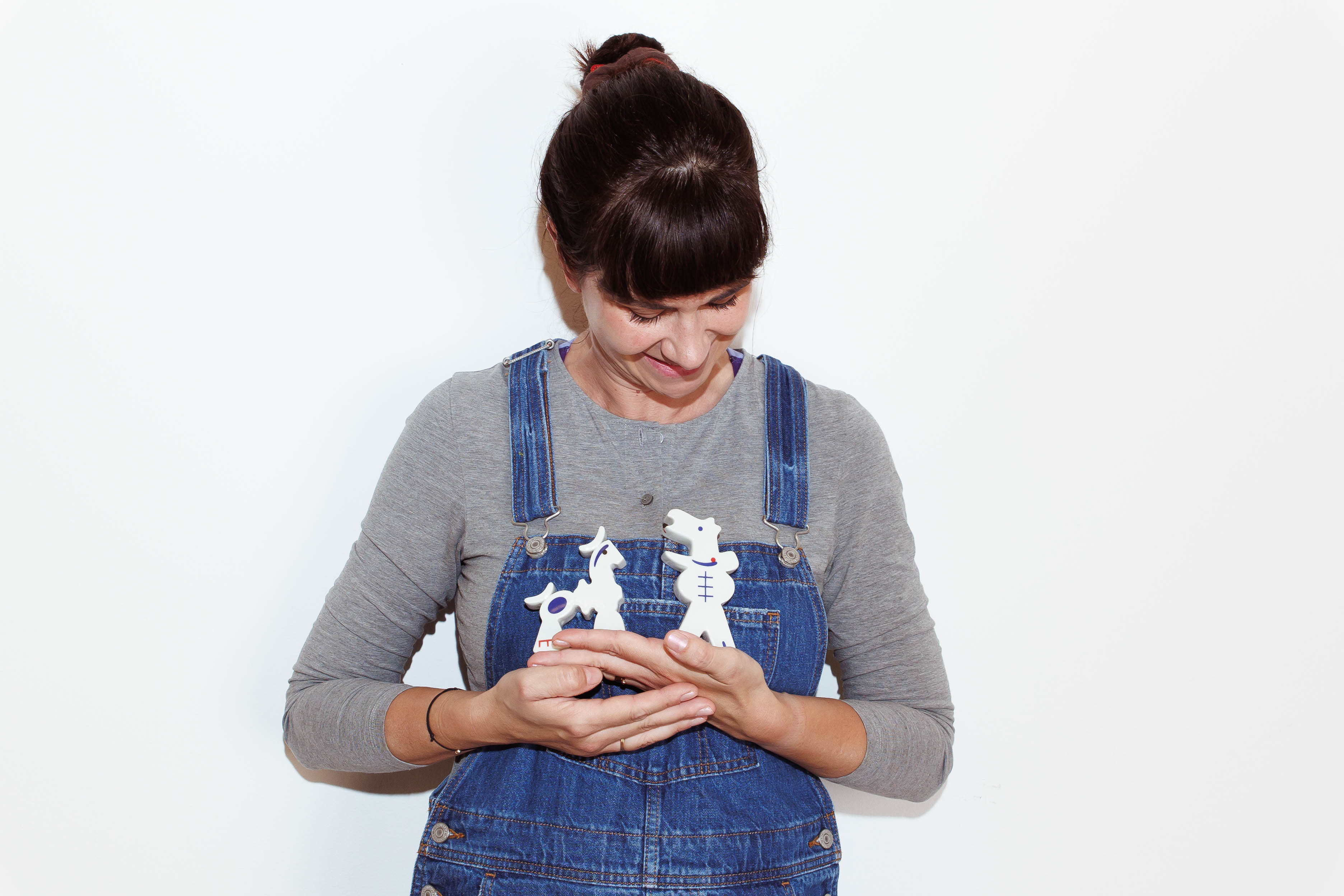 Tri porcelánové figúrky z kolekcie hračka-sochy – koník, sliepočka a mužská postava – prezentované v náručí autorky.