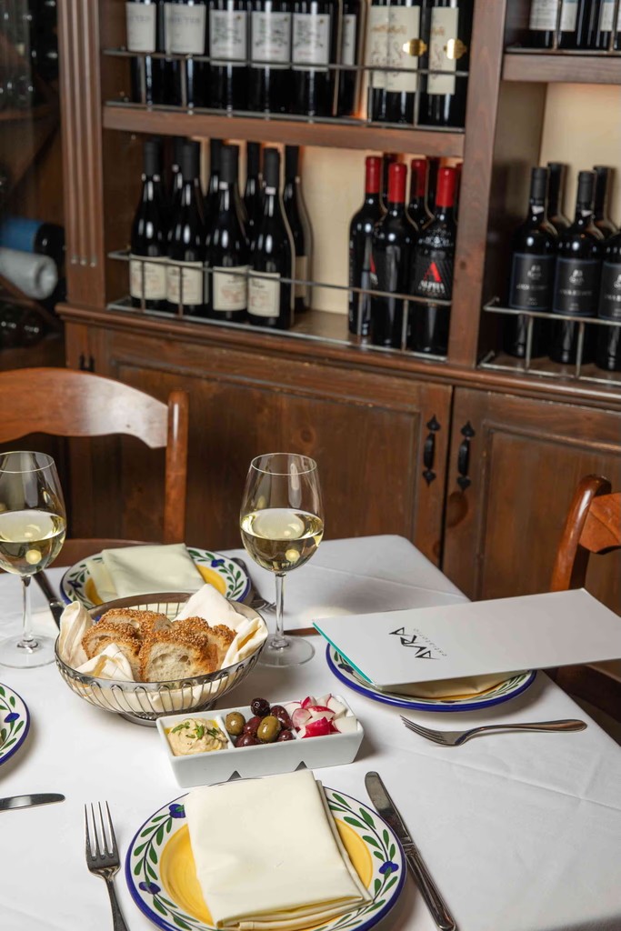 A dining table set with plates, glasses, and cutlery, surrounded by shelves filled with wine bottles.