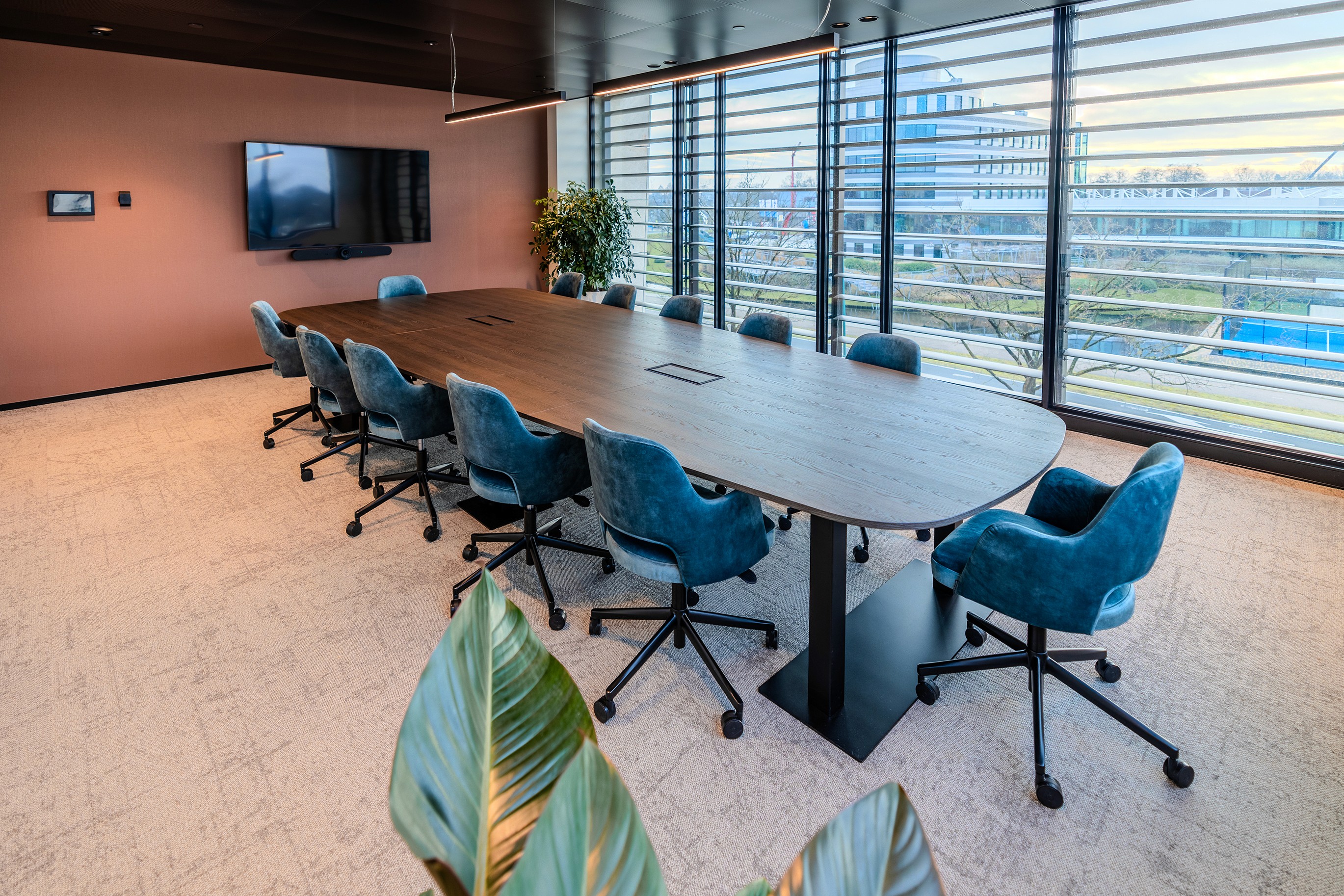 Formele vergaderruimte in AFAS DotNL met een ovale zwarte tafel, blauwe velour stoelen, een groot beeldscherm en panoramische raamwand met buitenzicht – DSN Workspace Solutions