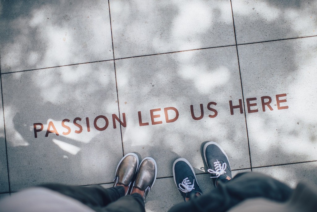 Inspirational quote "Passion Led Us Here" on sidewalk with shoes visible.