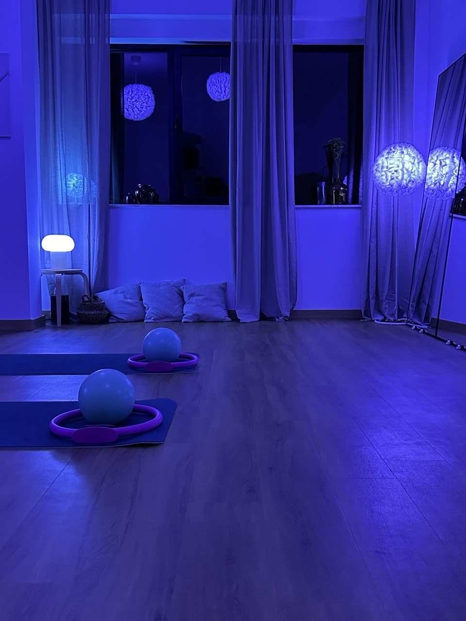 The Pilates studio illuminated by calming blue mood lighting, with exercise balls and Pilates rings placed on mats ready for a session.