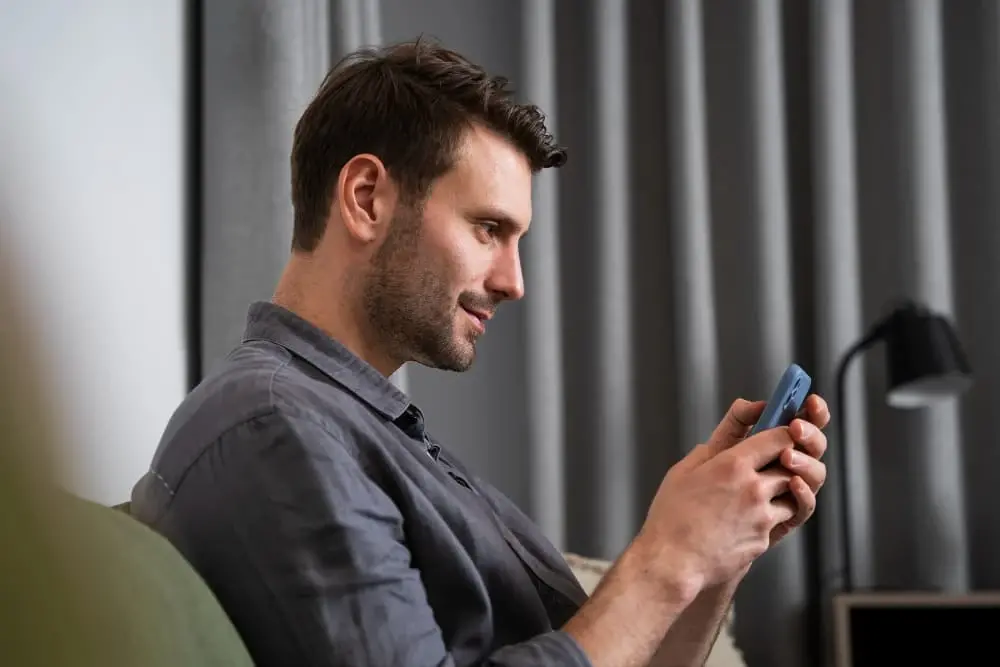 A man sits comfortably on a couch, smiling as he looks at his phone. The relaxed, modern setting suggests someone learning or exploring home loan options online with ease and confidence.