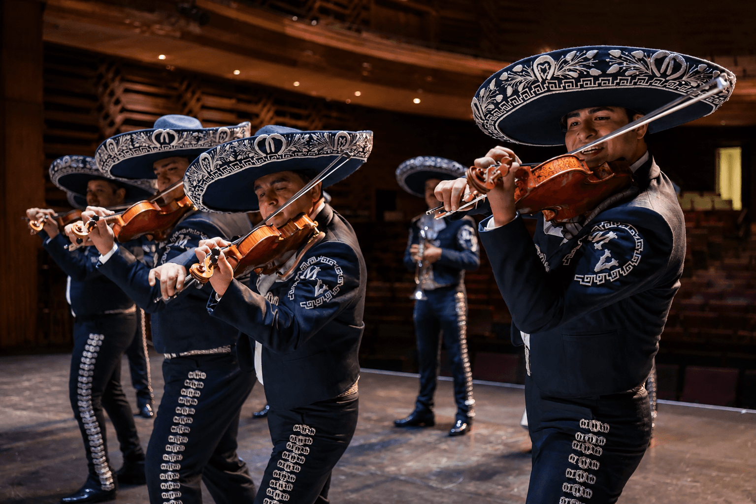 Músicos de mariachi interpretando violines con traje tradicional.
