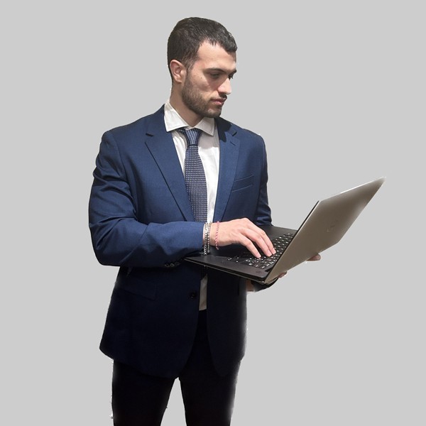 A confident person with short, styled hair and a leather jacket poses against a dark backdrop.