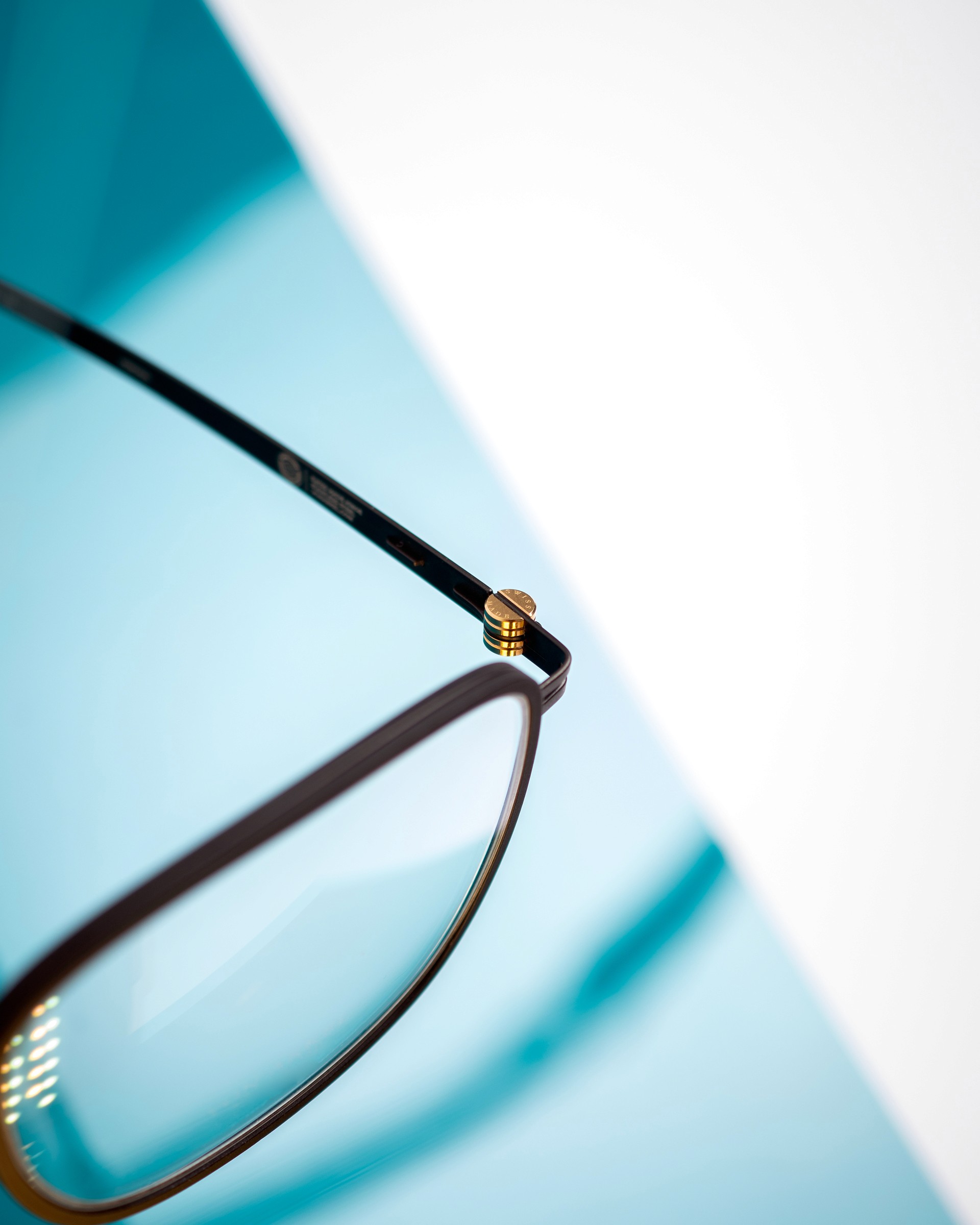 Photo studio macro sur un fond blanc et bleu ciel d'une charnière dorée de lunette de vue design de la marque Von Arkel