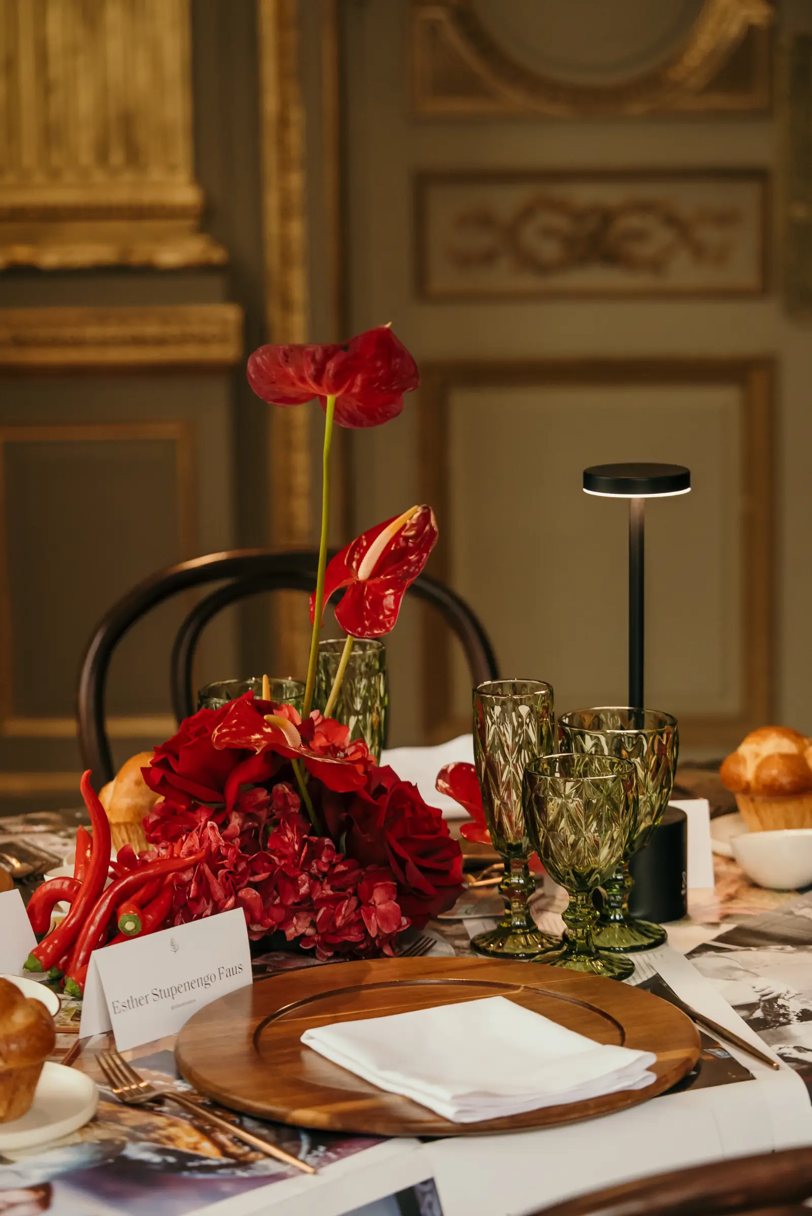 Sitting de mesa con nombre, rosas, chiles rojos, copas de cristal verde y lámpara LED de diseño minimalista.