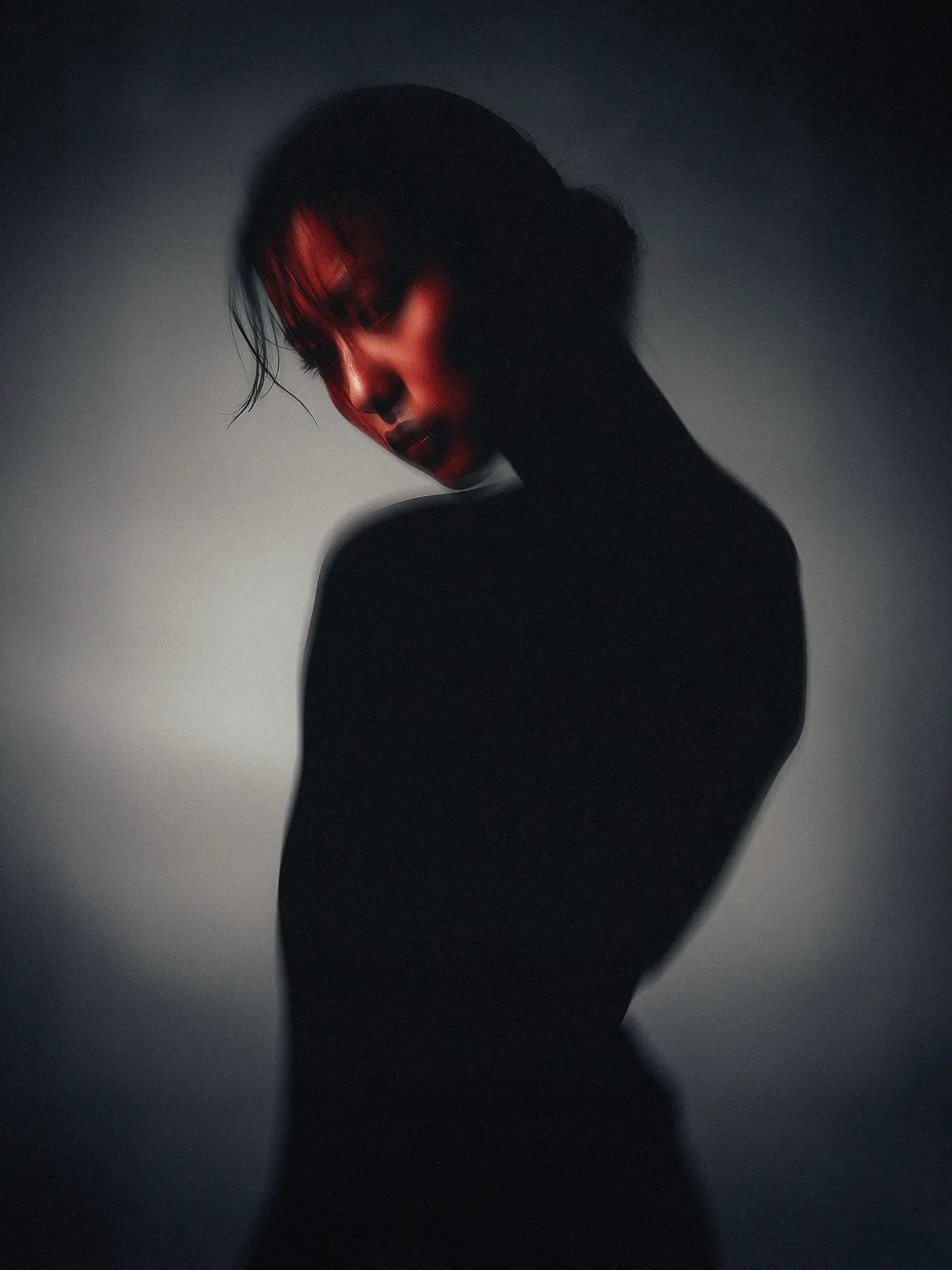 Portrait with bowed head and a black high-neck garment in a circular pool of light.