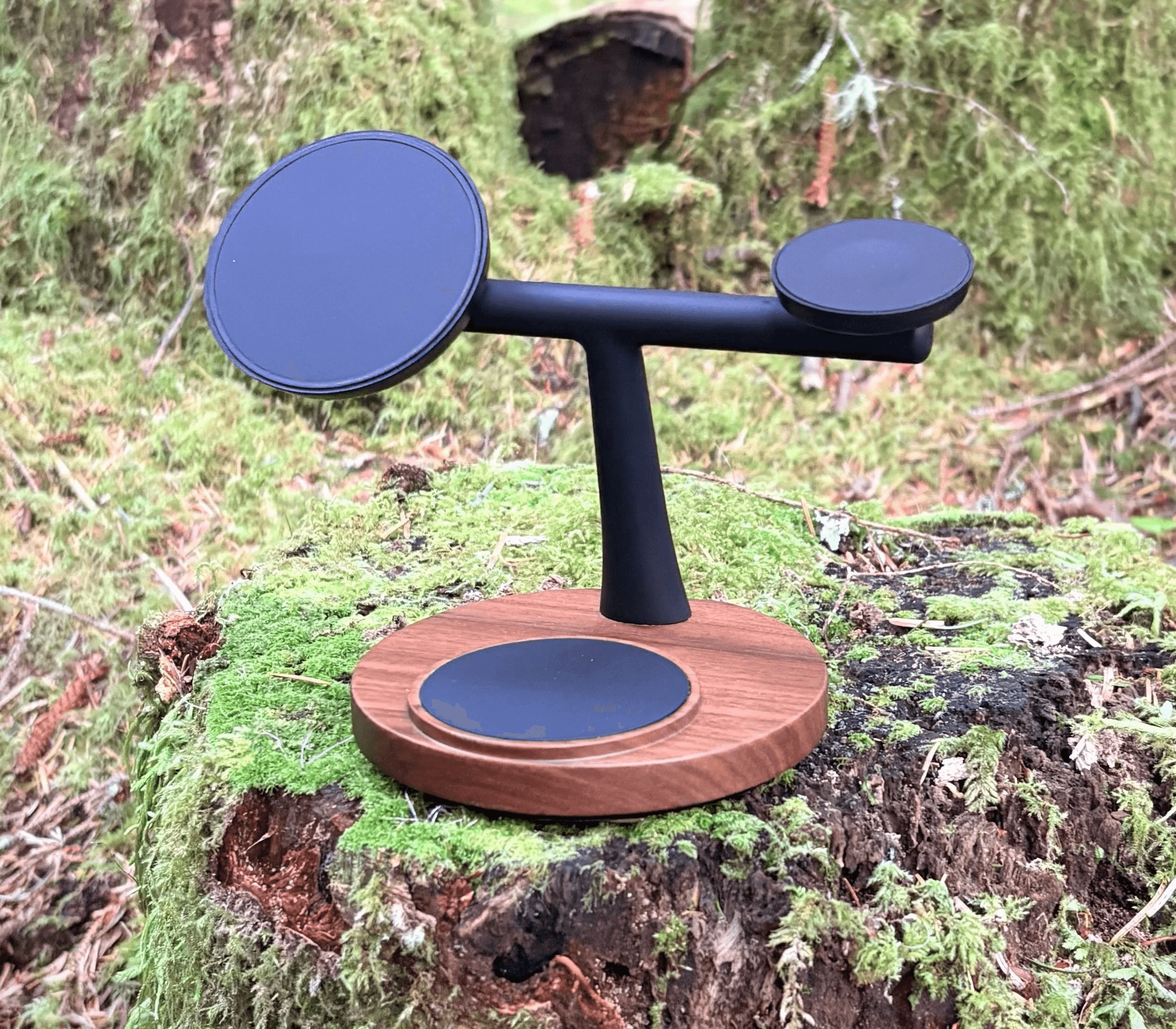 A sleek black and brown ZenStand wireless charging station rests on a moss-covered tree stump, blending stylishly with the natural forest surroundings.