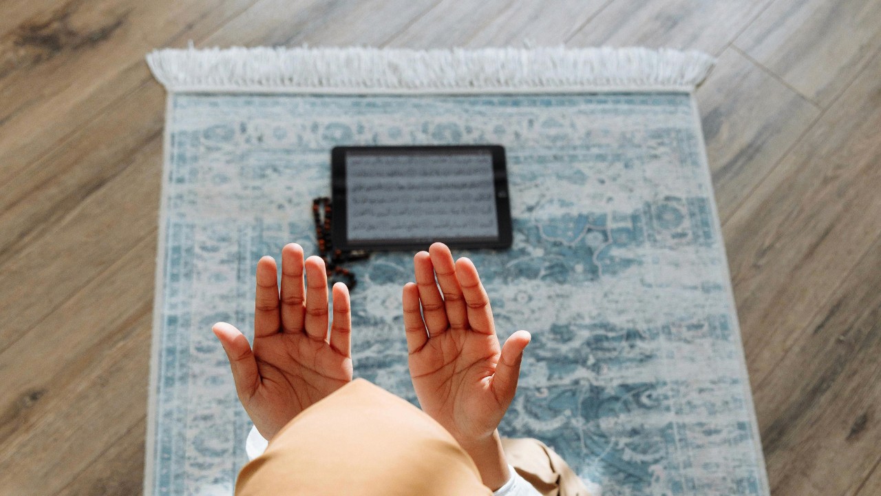 An image showing hands making dua in front of a prayer mat