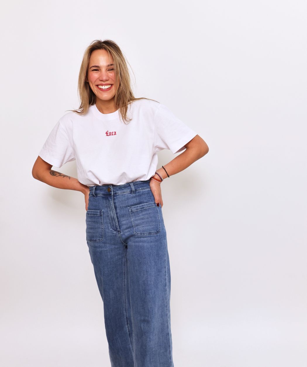 Smiling-model-wearing-a-white-Luca-logo-t-shirt-with-a-small-red- script-logo-and-wide-leg-denim-jeans