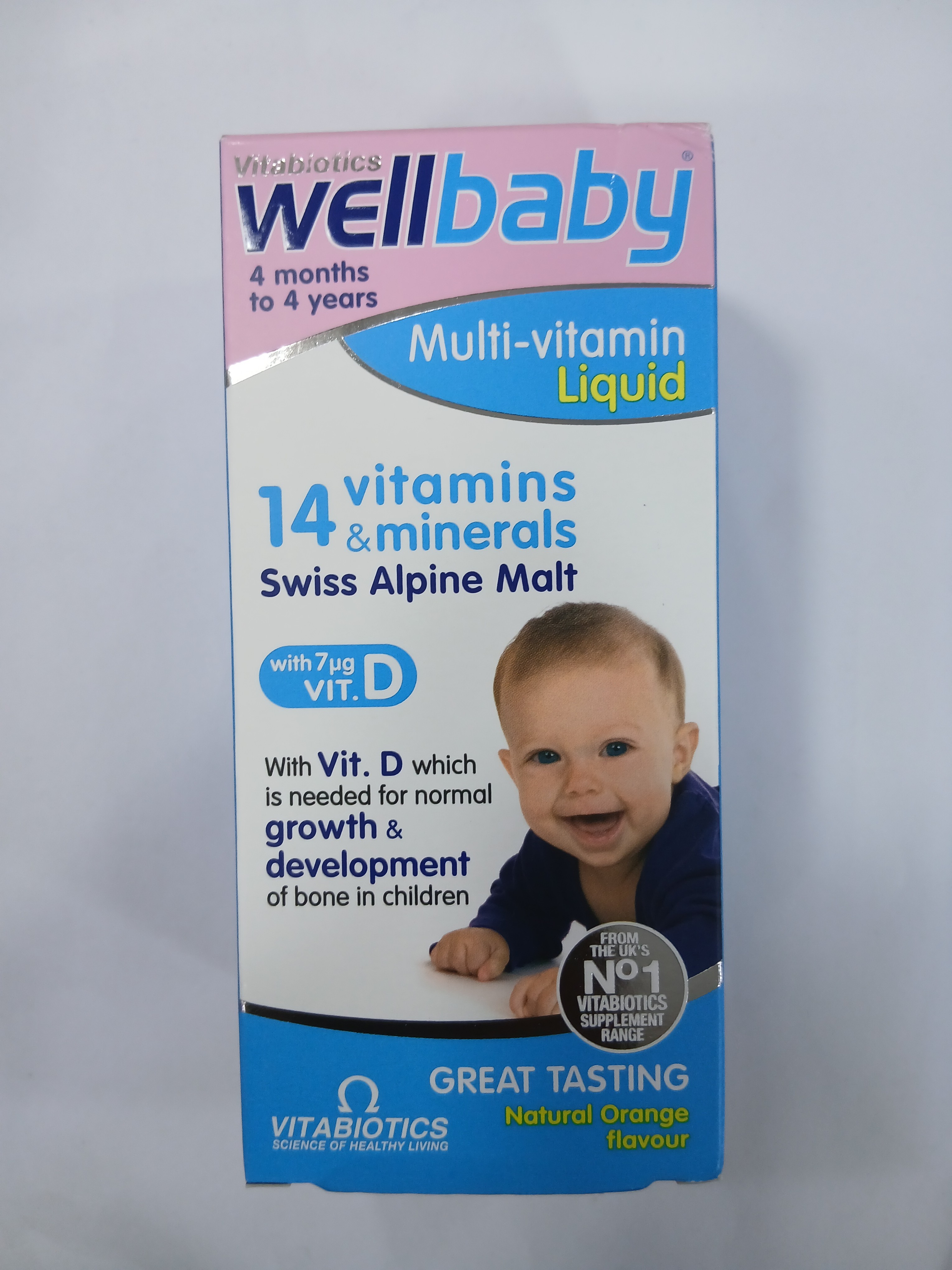 White cardboard box packaging for a multi-vitamin liquid supplement displays a smiling baby lying on a light-colored surface, with text indicating it contains 14 vitamins and minerals including Swiss Alpine Malt and vitamin D.