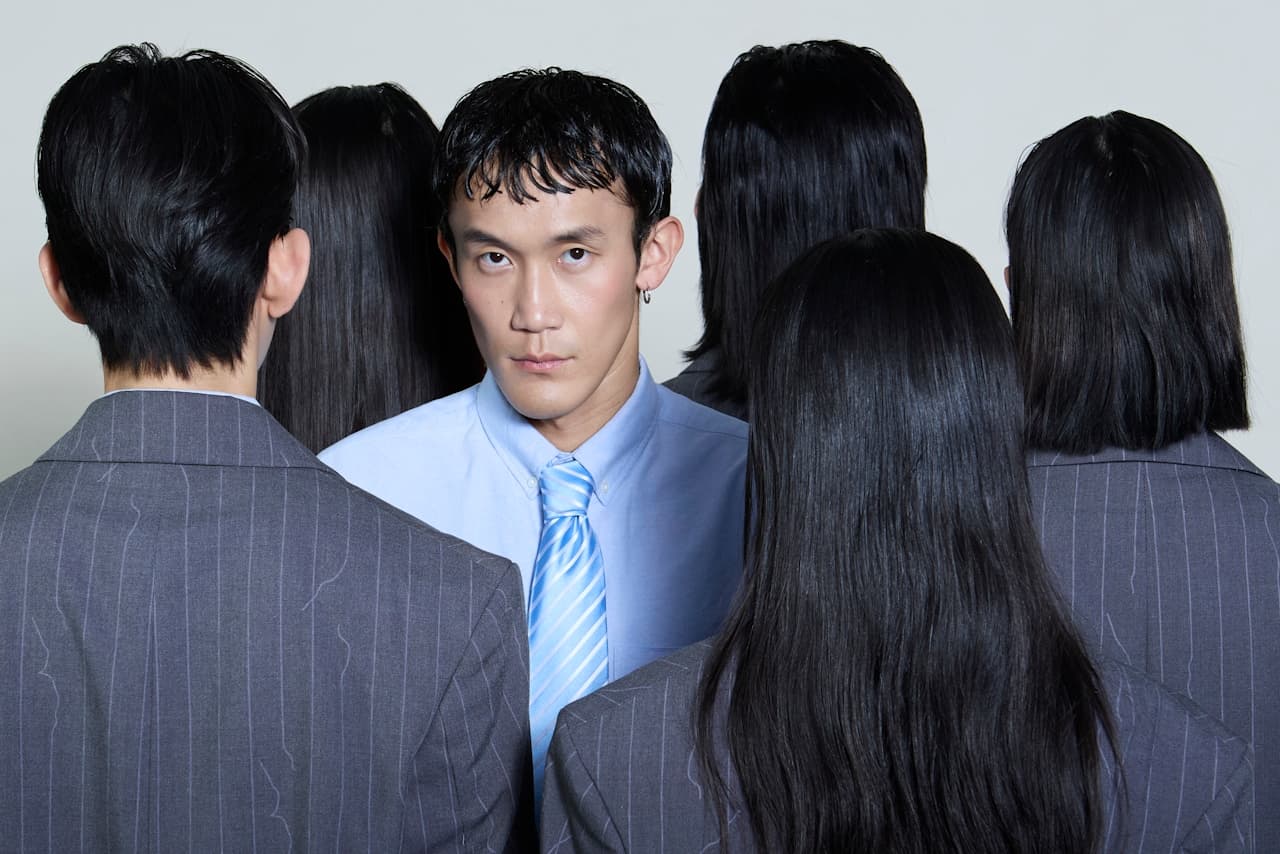 A man wearing a suit and tie staring directly at the viewier, among colleagues that are facing the other way.
