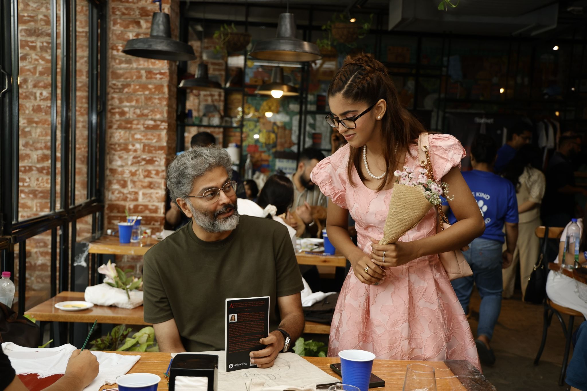 Raj Lakshmi Sharma holds flowers while speaking with an attendee at a book event.