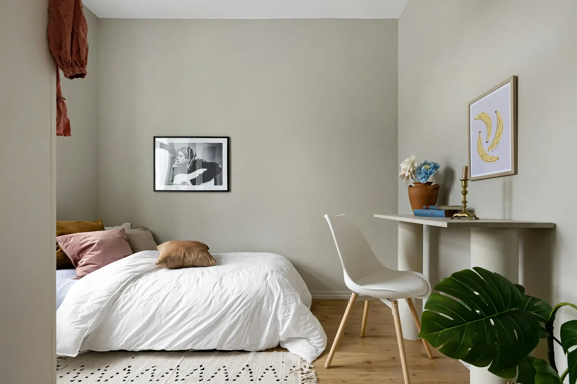 Simple bedroom with white bedding, small desk, framed art, and indoor plant.