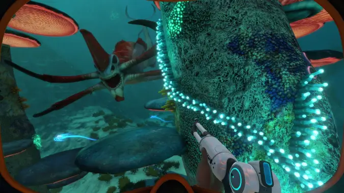 A person in a futuristic submarine suit points a high-tech tool towards a menacing sea creature with sharp teeth, swimming amidst large, colorful coral structures in an underwater environment.