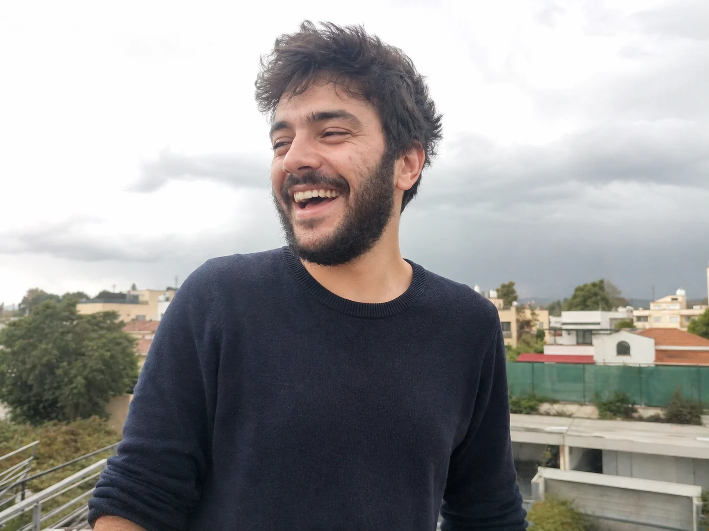 Smiling young man outdoors with cloudy skies and city buildings in the background