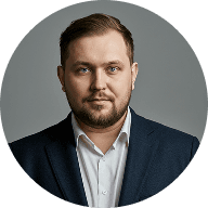 A bearded man in a suit gazes directly at the camera with a confident expression.