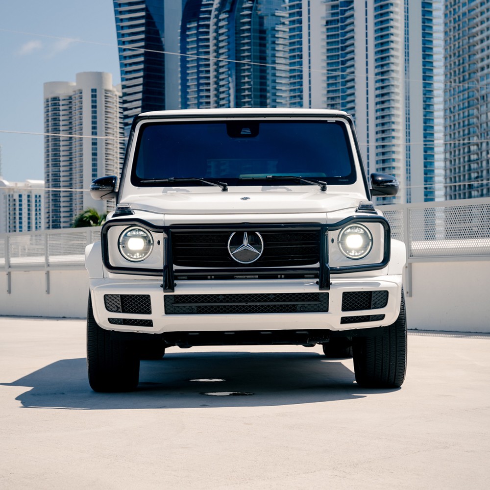 Head-on front view of a white Mercedes-Benz G 550 (G-Wagon), emphasizing its bold grille and round LED headlights.