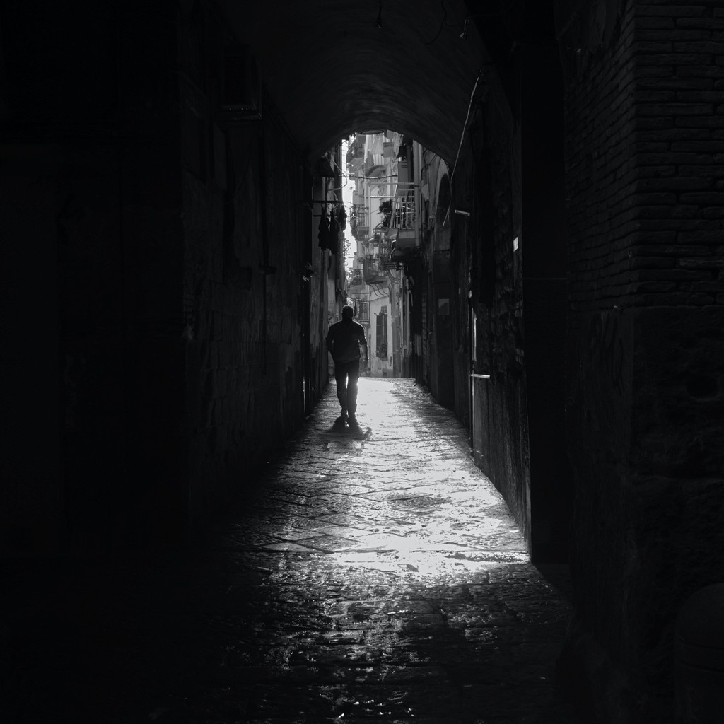 black white image showing a man walking away from the camera in a dark alley.