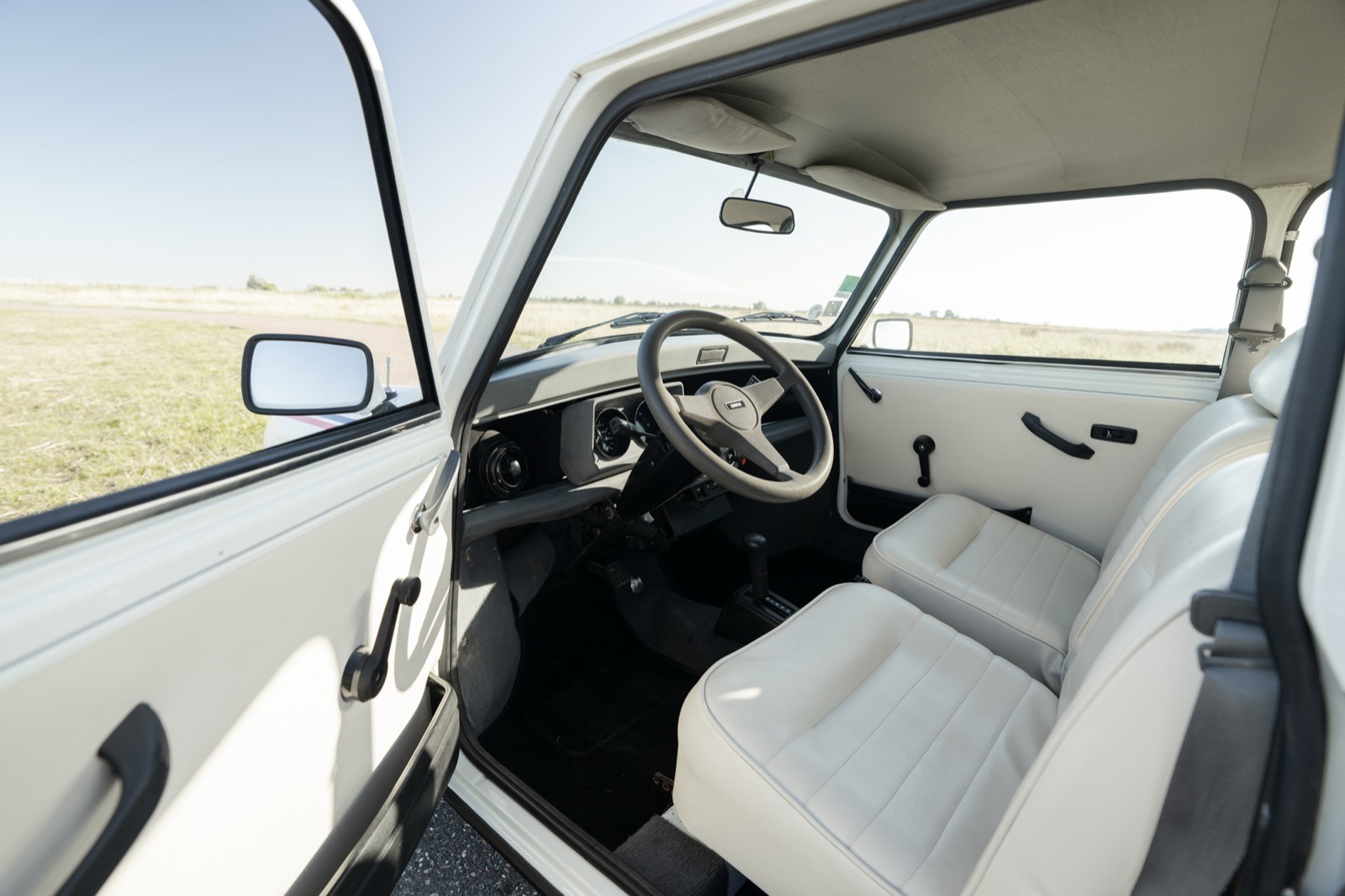 Interior view of a car showcasing a clean white seat, steering wheel, and dashboard against an open landscape.