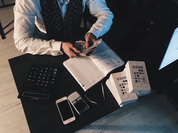 Person counting money at a desk with a calculator and notebook, representing bookkeeping tasks.